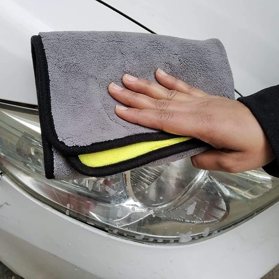 Gray microfiber cleaning cloth with black border being smoothed on a car headlight