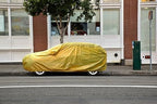 All weather car cover, yellow, full coverage over car parked by building